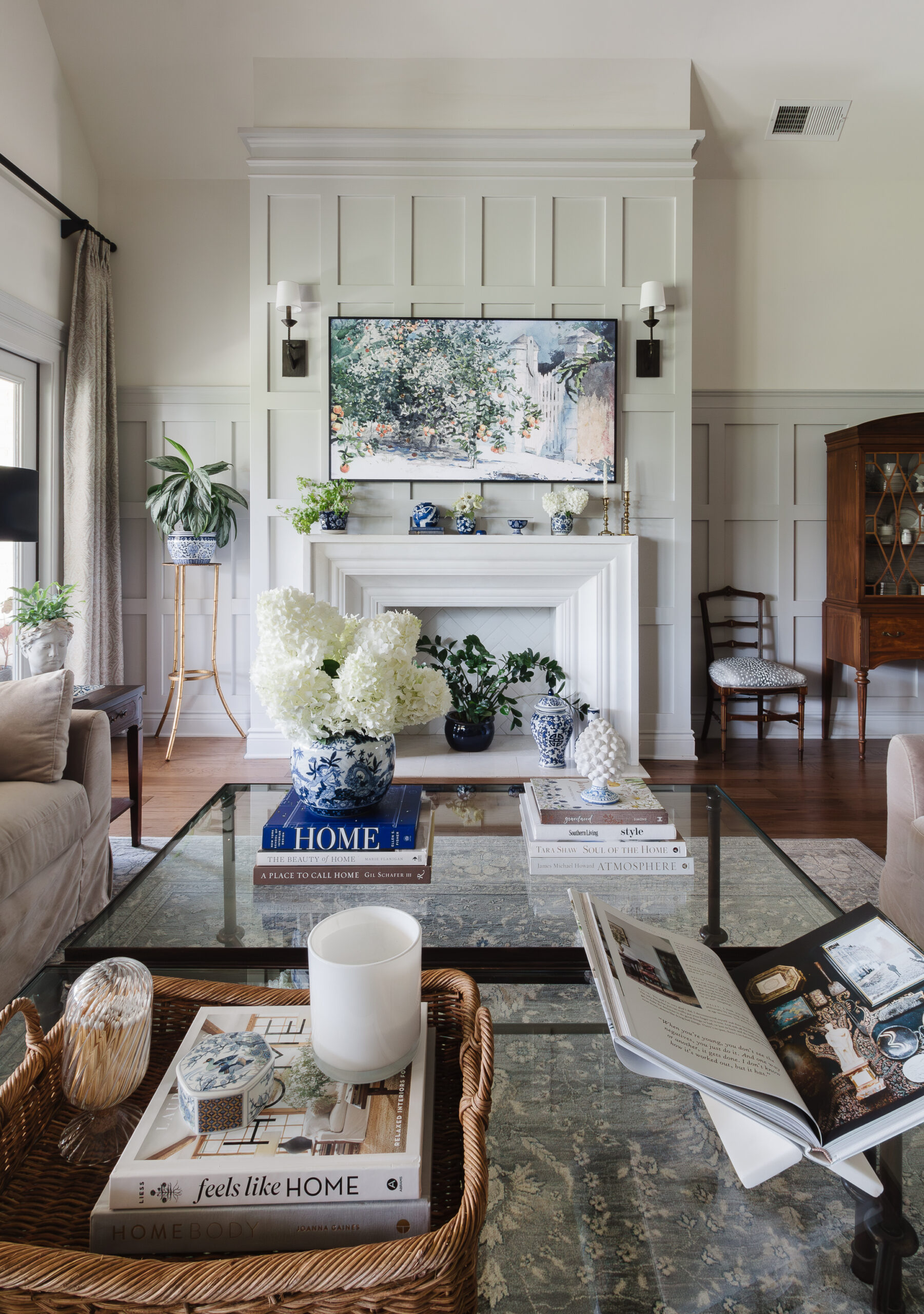 Living room with a white paneled fireplace, TV mounted above, and blue‑and‑white ceramics on the mantel flanked by wall sconces.