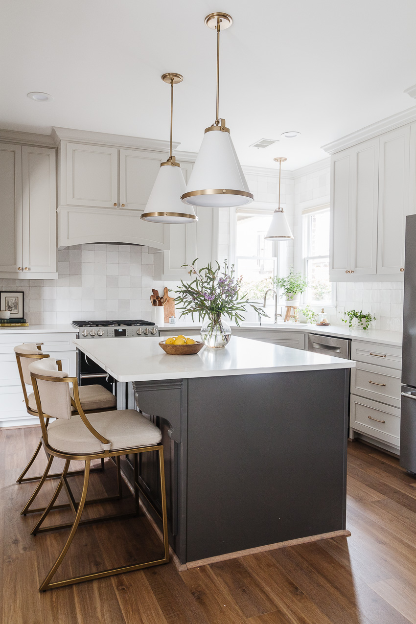Bright white kitchen with a large central island, gold-accent pendant lights, and dark wood floors.